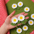 Crochet daisy fridge magnet held in hand, showing handmade white and yellow flower detail