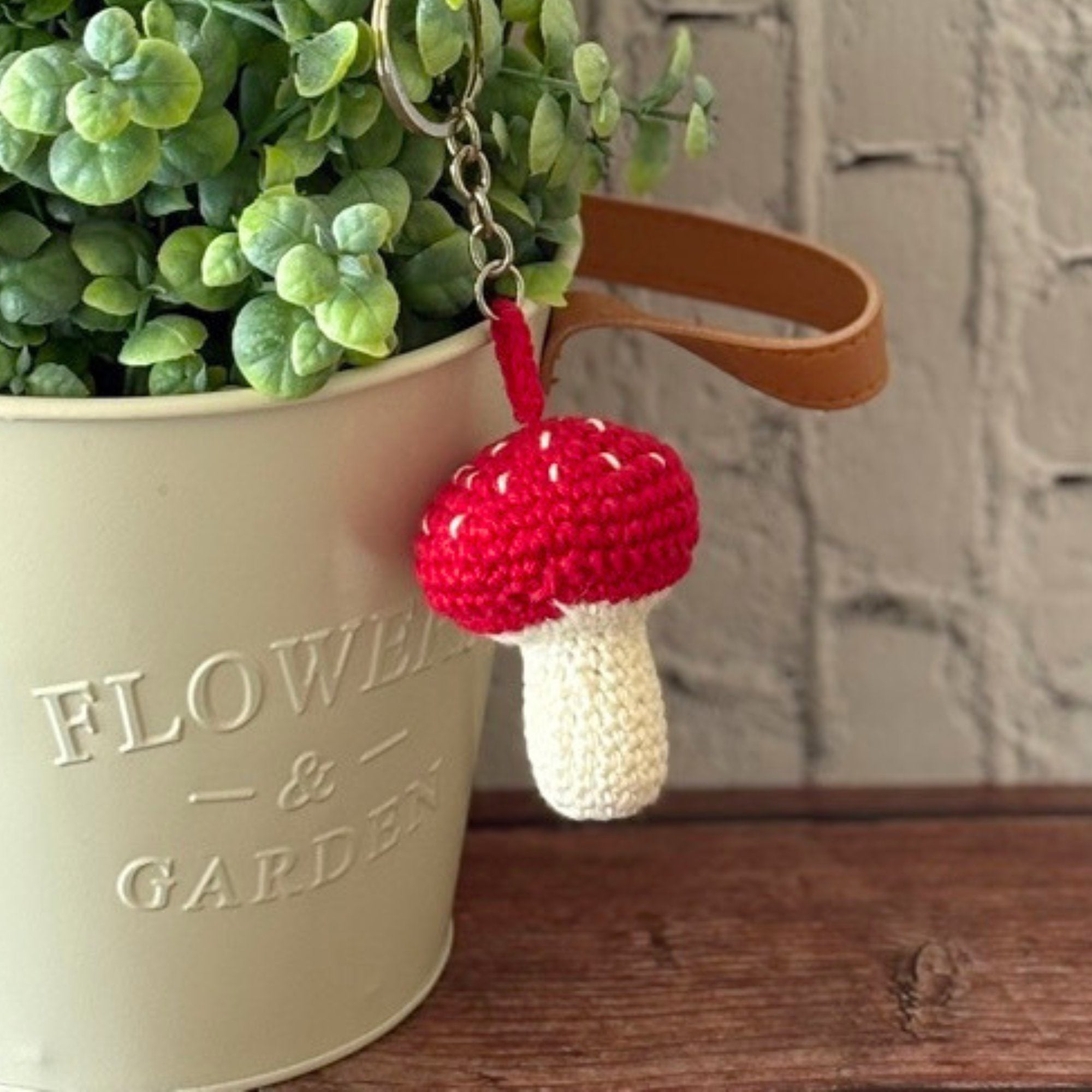 Crochet red mushroom keychain next to a plant pot, handmade in Toronto